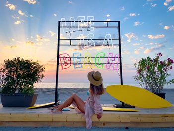 Fashionable young woman on the beach sitting under a colorful neon sign