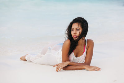 Portrait of young woman lying on sand at beach against sky