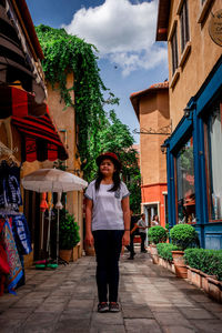 Woman wearing hat while standing on footpath amidst buildings