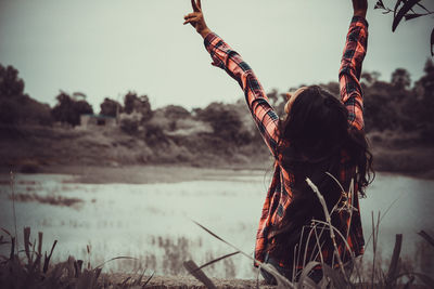 Rear view of woman with arms raised sitting against lake