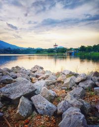 Rocks by lake against sky during sunset