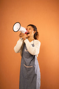 Portrait of young woman drinking bottles against yellow background