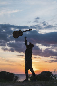 Man throwing guitar while standing on beach during sunset