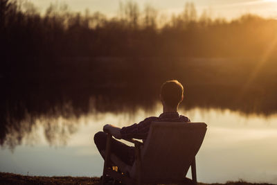 Rear view of silhouette man sitting on bench