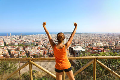 Full length of young woman standing on railing against cityscape of barcelona, spain