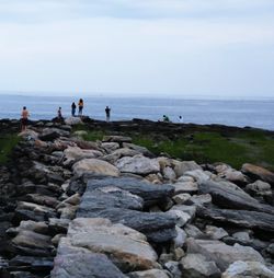 People on rocks by sea against sky