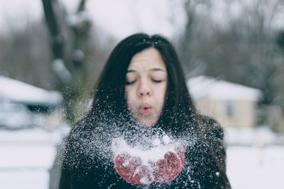 Close up of young woman blowing snow during winter