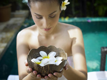 Woman holding frangipani in container at poolside