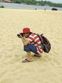 Man photographing through camera while crouching on sand at beach