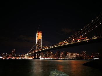 Illuminated bridge over river in city at night