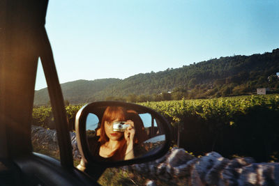 Reflection of man photographing car on side-view mirror