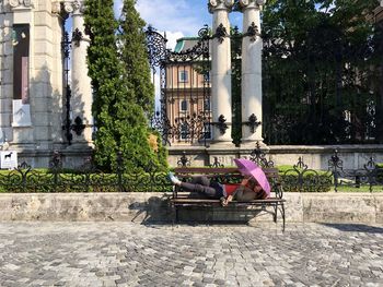 Man sitting by statue in city against sky