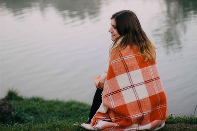 Young woman with blanket sitting on lakeshore