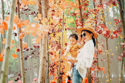 Smiling mother with son standing against autumn tree in forest