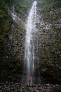 Rear view of man looking at waterfall falling from mountain in forest