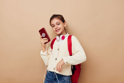 Portrait of girl with smart phone standing against beige background