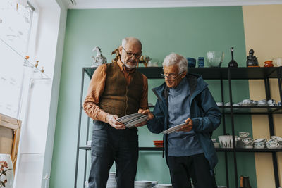 Male customer examining plates held by salesman in antique shop