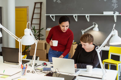 Female business coworkers discussing over laptop at desk in creative office