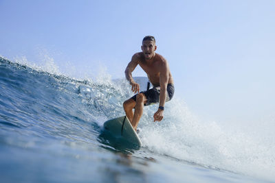 Carefree shirtless man surfing on sea wave against clear sky