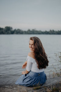 Woman sitting in lake against sky