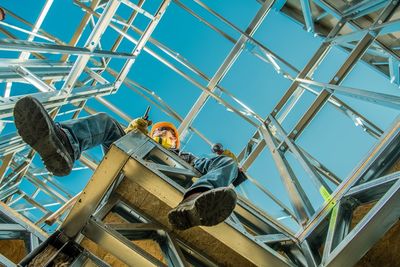 Low angle view of man sitting at construction site against sky