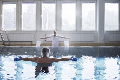 Shirtless man exercising with dumbbells in swimming pool at rehabilitation center