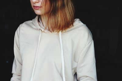 Midsection of woman wearing white hooded shirt against black background