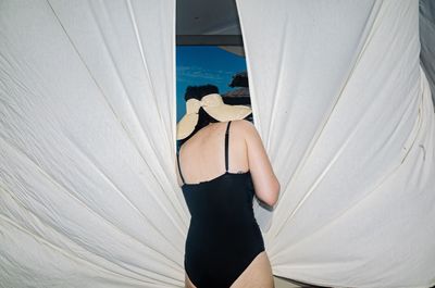 Rear view of woman standing against white curtain