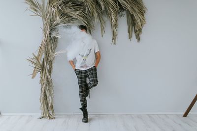 Man with smoke standing against white wall