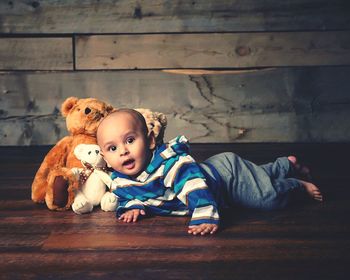 Side view portrait of baby boy lying by teddy bears on hardwood floor