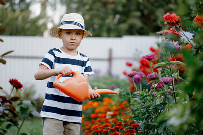 Cute little boy watering flowers with a watering can on a sunny summer day