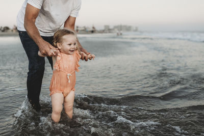 Toddler girl splashing in ocean with father at sunset