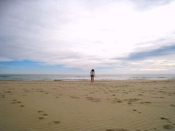 Woman walking on beach against cloudy sky