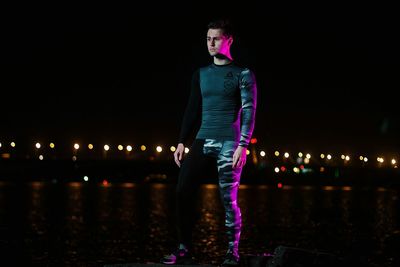 Young man standing against illuminated lights at night