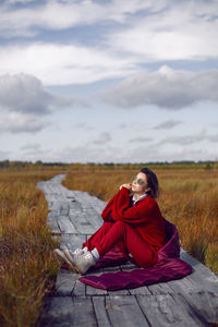 Woman  in red warm clothes and a big scarf on an ecological trail in the autumn not a swamp