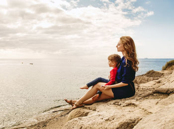 Mother and son sitting on beach against sky