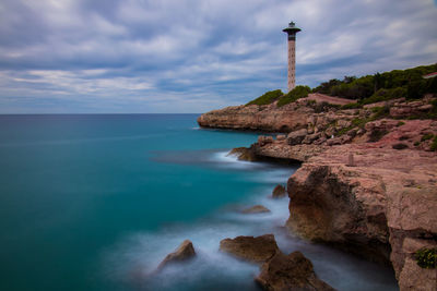 Lighthouse on rocks by sea against sky