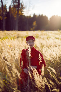 Woman in a red sweater cap and scarf stands in a field in autumn in the tall dry grass
