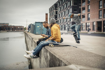 Male friend looking while man skating on footpath by canal