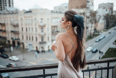 Side view of young woman standing on railing in city