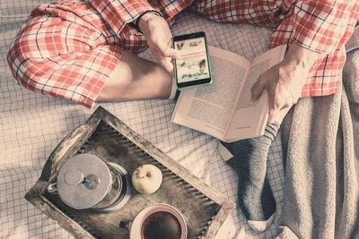 High angle view of man using phone sitting by coffee on bed