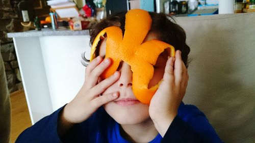 Close-up of boy playing with orange peel at home