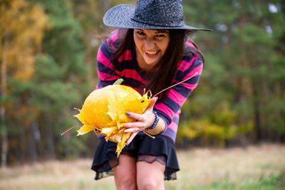 Young woman in black dress with witch hat and orange pumpkin placed around in the forest,