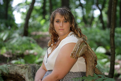 Portrait of young woman sitting on log in forest