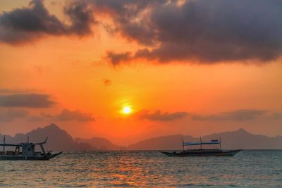 Boats sailing on sea against orange sky