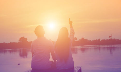 Rear view of people in lake against sky during sunset