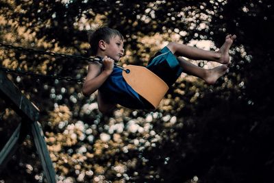 Side view of boy playing on swing at park