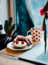 Midsection of a person with coffee cup, cherry tart and laptop on  a wooden table