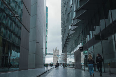 People walking on street amidst buildings against tower bridge in city