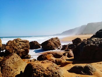 Rocks on beach against clear blue sky